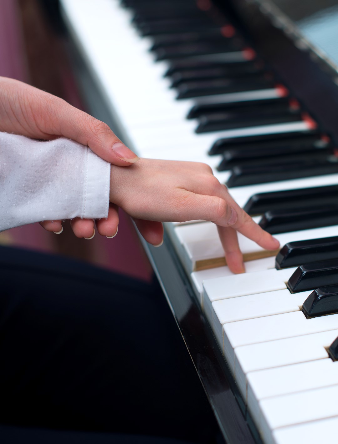 Woman teaching little girl to play the piano.